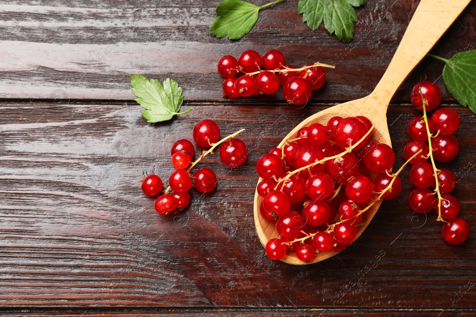 Photo of Fresh red currants and green leaves on wooden table, flat lay. Space for text