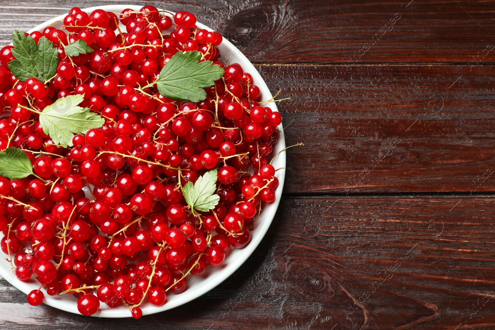 Photo of Fresh red currants and leaves on wooden table, top view. Space for text