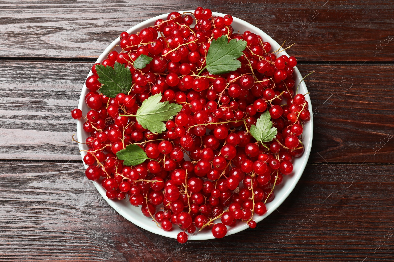 Photo of Fresh red currants and green leaves on wooden table, top view