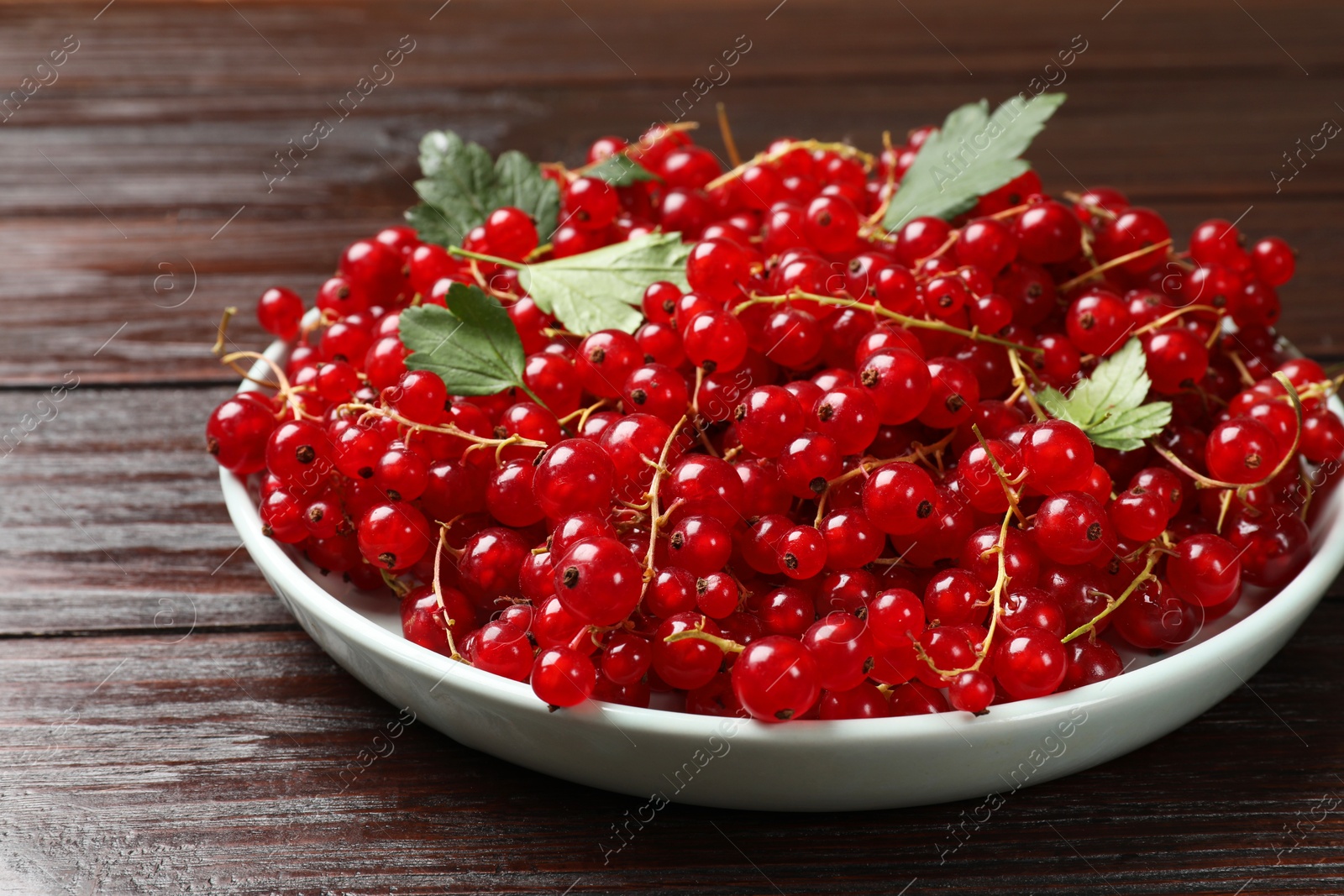 Photo of Fresh red currants and leaves on wooden table, closeup