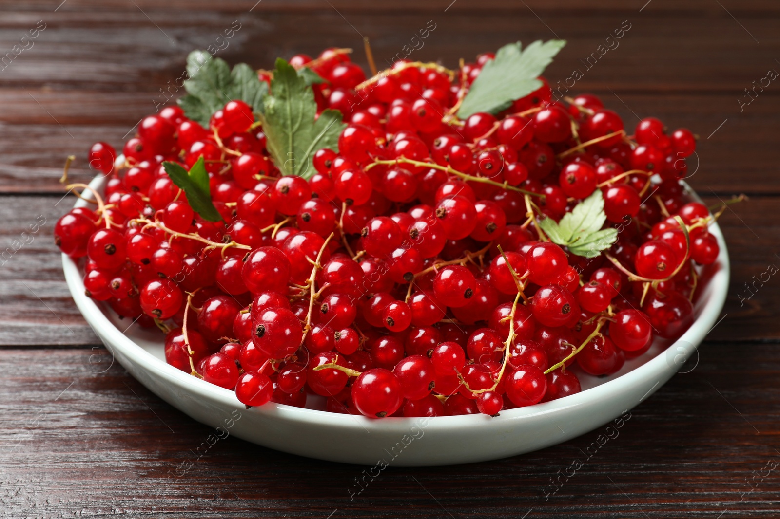 Photo of Fresh red currants and leaves on wooden table, closeup