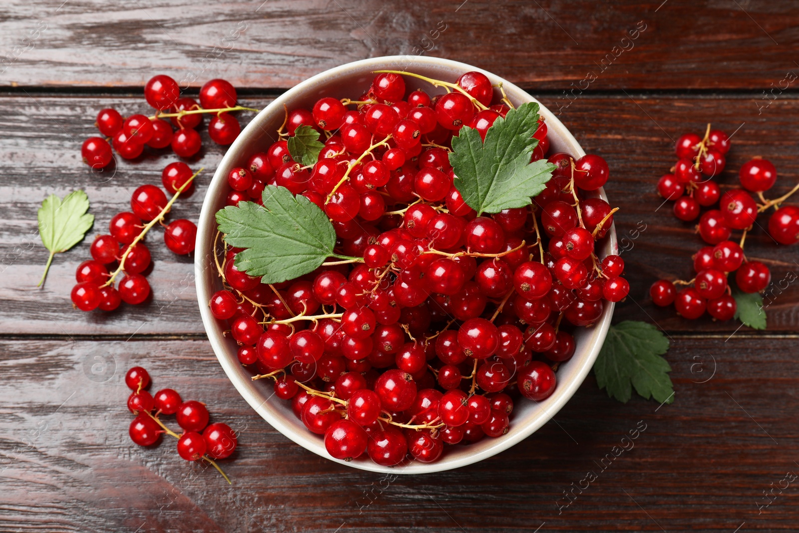 Photo of Fresh red currants in bowl and green leaves on wooden table, top view