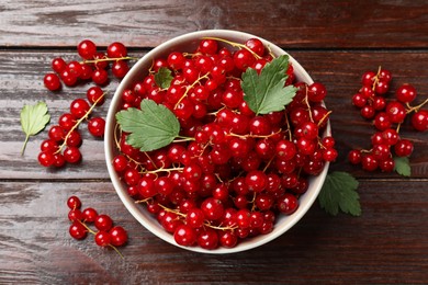 Photo of Fresh red currants in bowl and green leaves on wooden table, top view