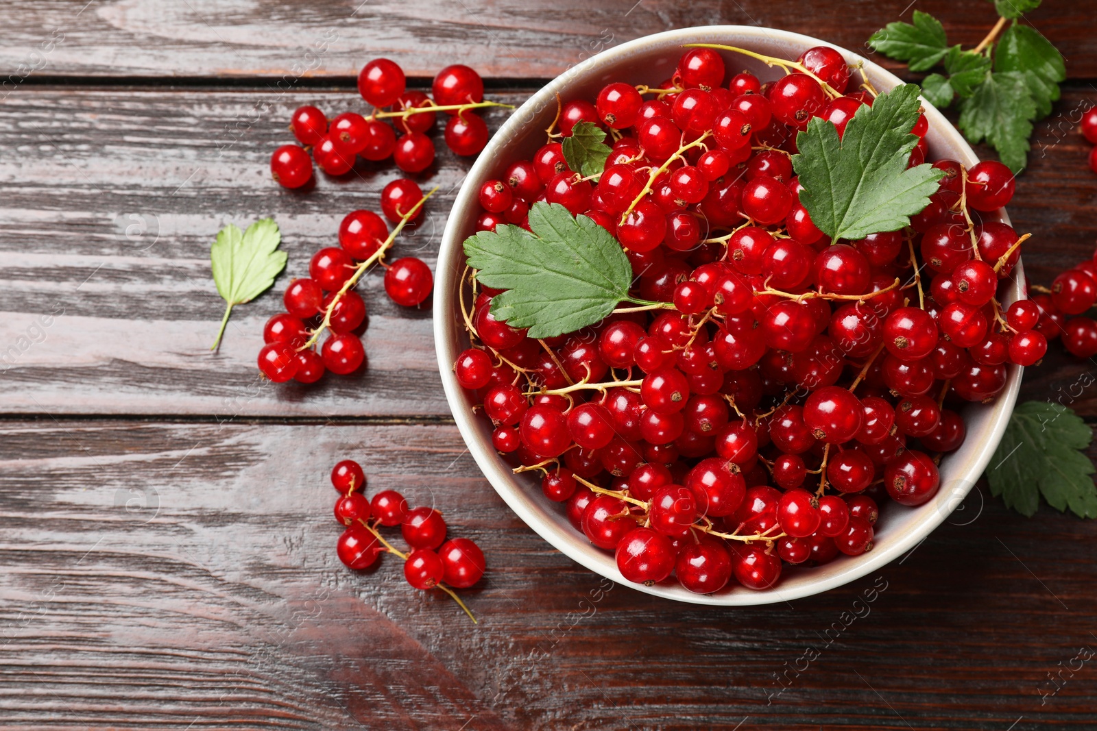 Photo of Fresh red currants in bowl and green leaves on wooden table, top view