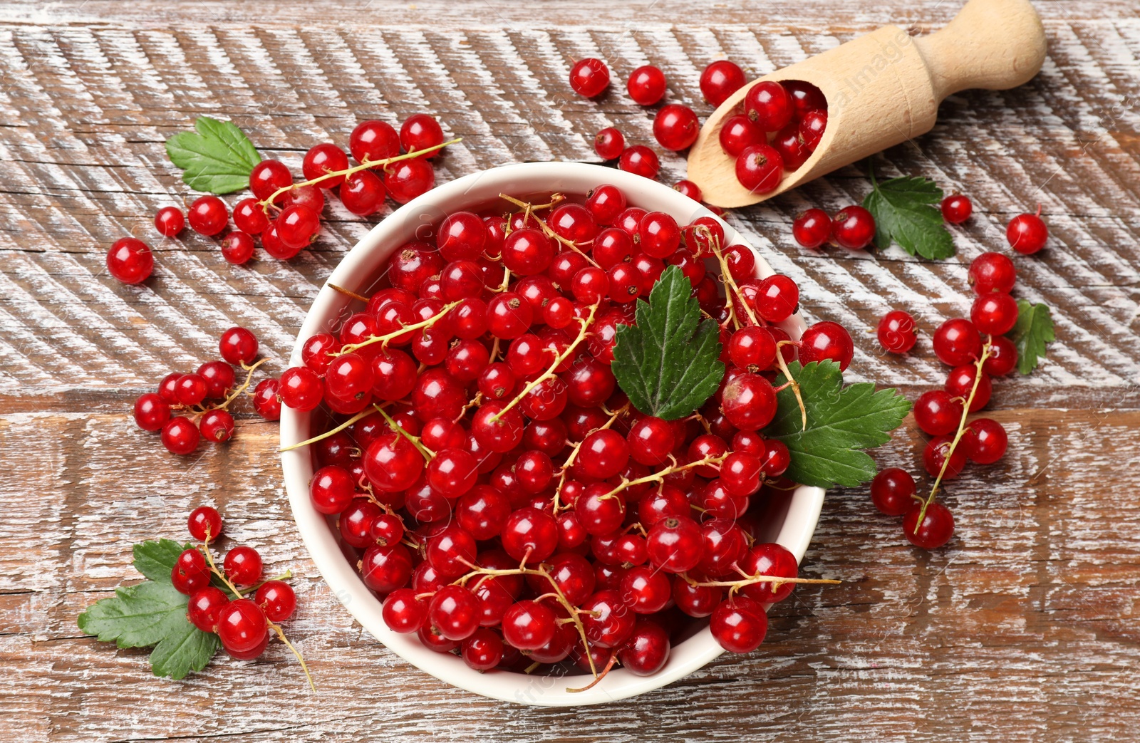 Photo of Fresh red currants and green leaves on wooden table, flat lay