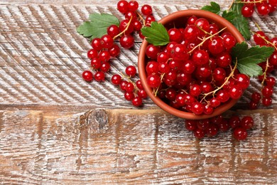 Photo of Fresh red currants in bowl and green leaves on wooden table, top view. Space for text