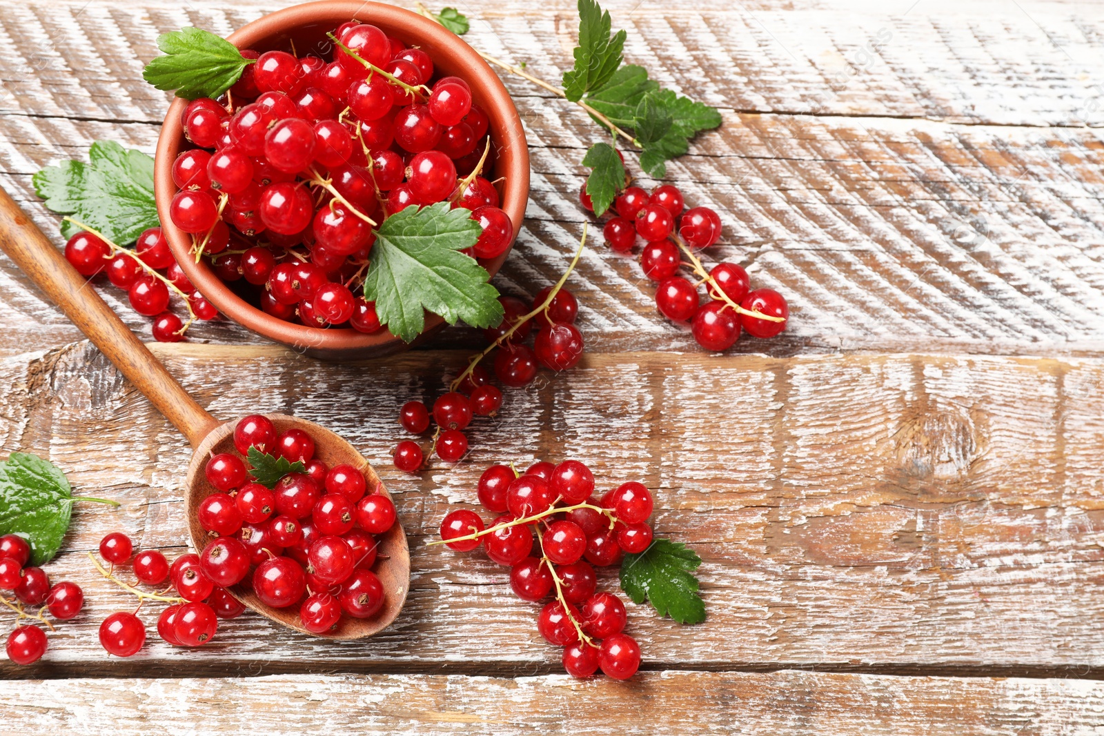 Photo of Fresh red currants and green leaves on wooden table, flat lay. Space for text