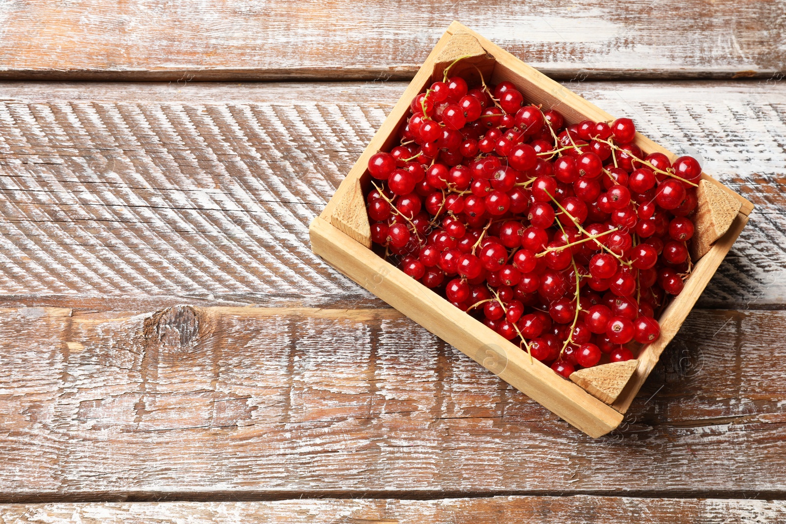 Photo of Fresh red currants in crate on wooden table, top view. Space for text