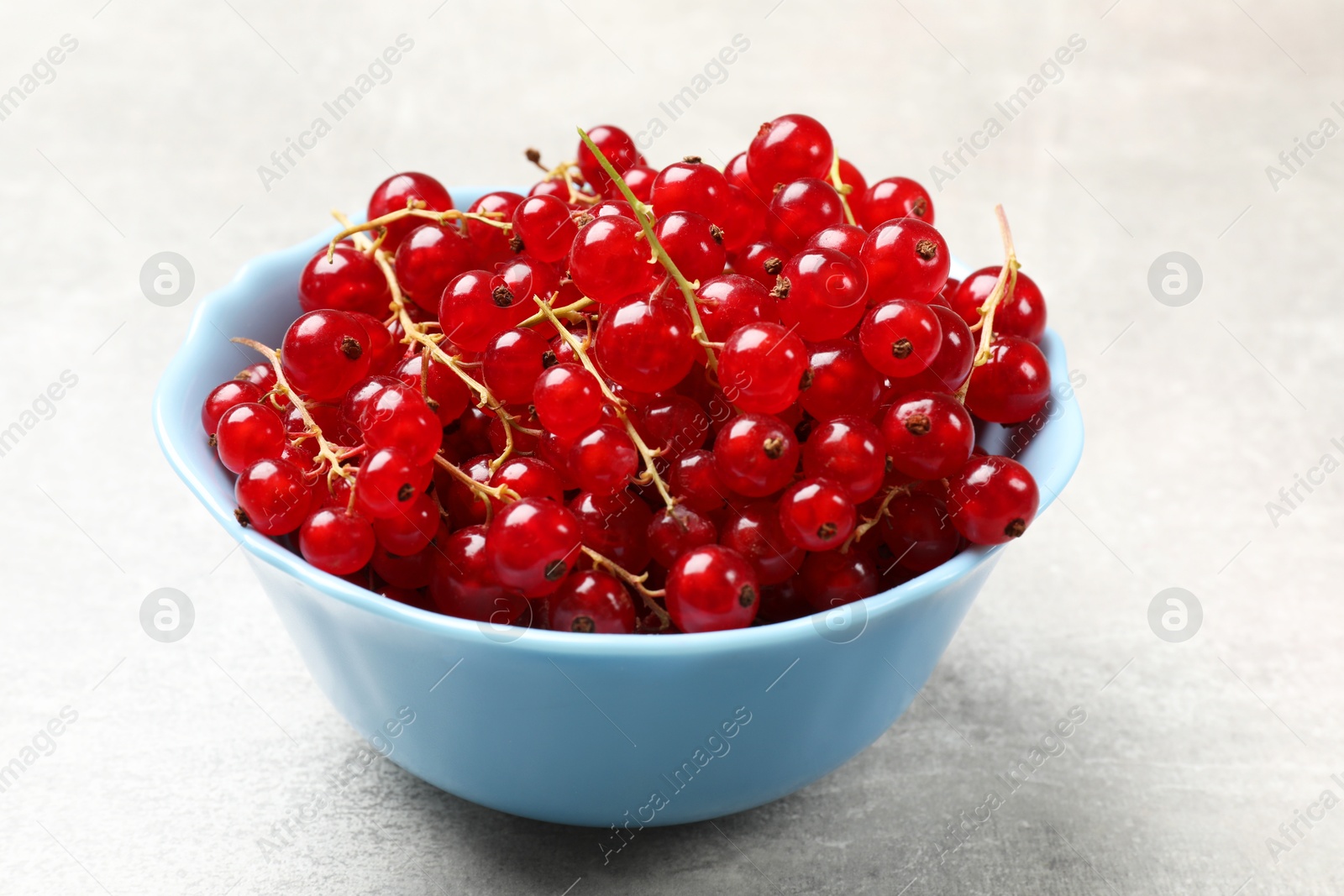 Photo of Fresh red currants in bowl on light grey table, closeup