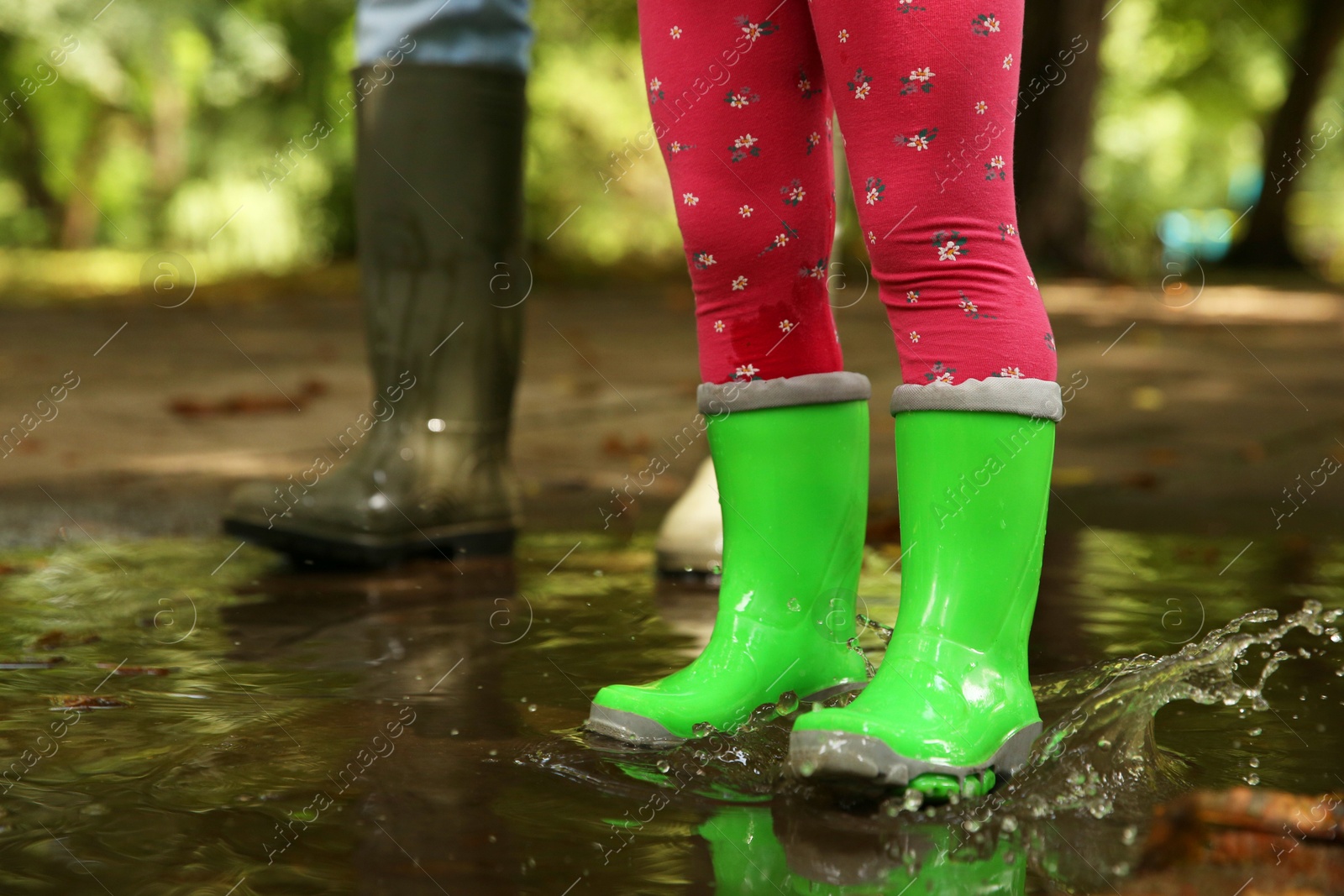 Photo of Mother and daughter wearing rubber boots standing in puddle outdoors, closeup