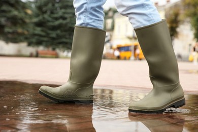 Woman wearing rubber boots walking in puddle outdoors, closeup