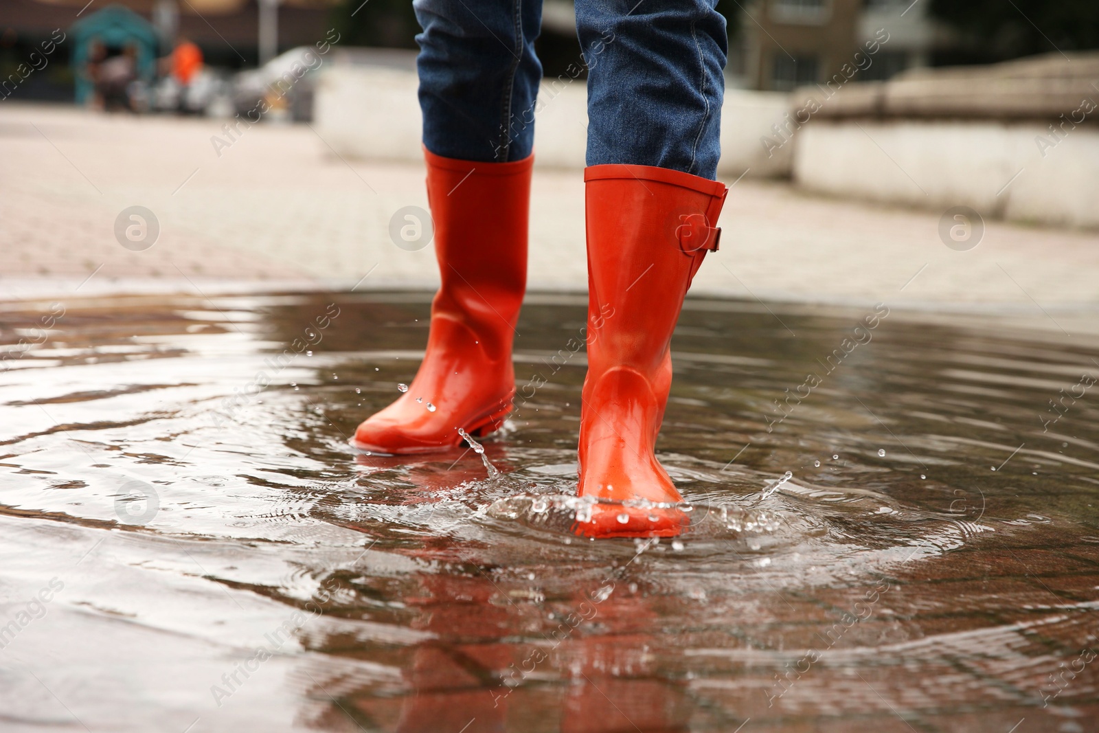 Photo of Woman wearing orange rubber boots standing in puddle outdoors, closeup