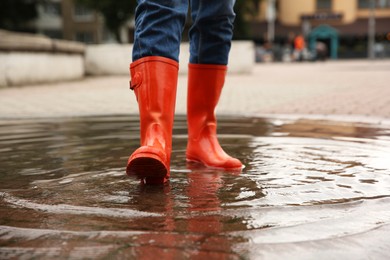 Woman wearing orange rubber boots standing in puddle outdoors, closeup