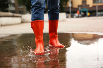 Photo of Woman wearing orange rubber boots standing in puddle outdoors, closeup