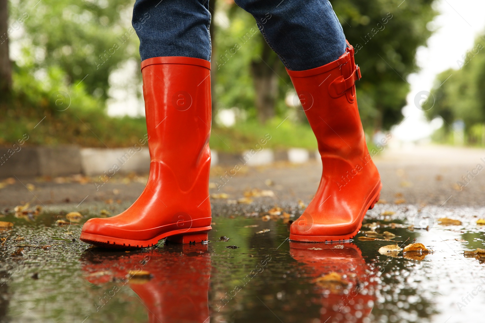 Photo of Woman wearing orange rubber boots walking in puddle outdoors, closeup