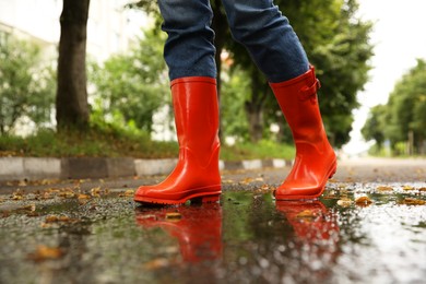 Photo of Woman wearing orange rubber boots walking in puddle outdoors, closeup