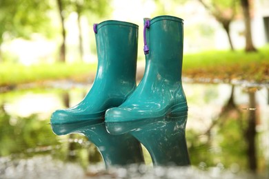 Photo of Pair of colorful rubber boots in puddle outdoors