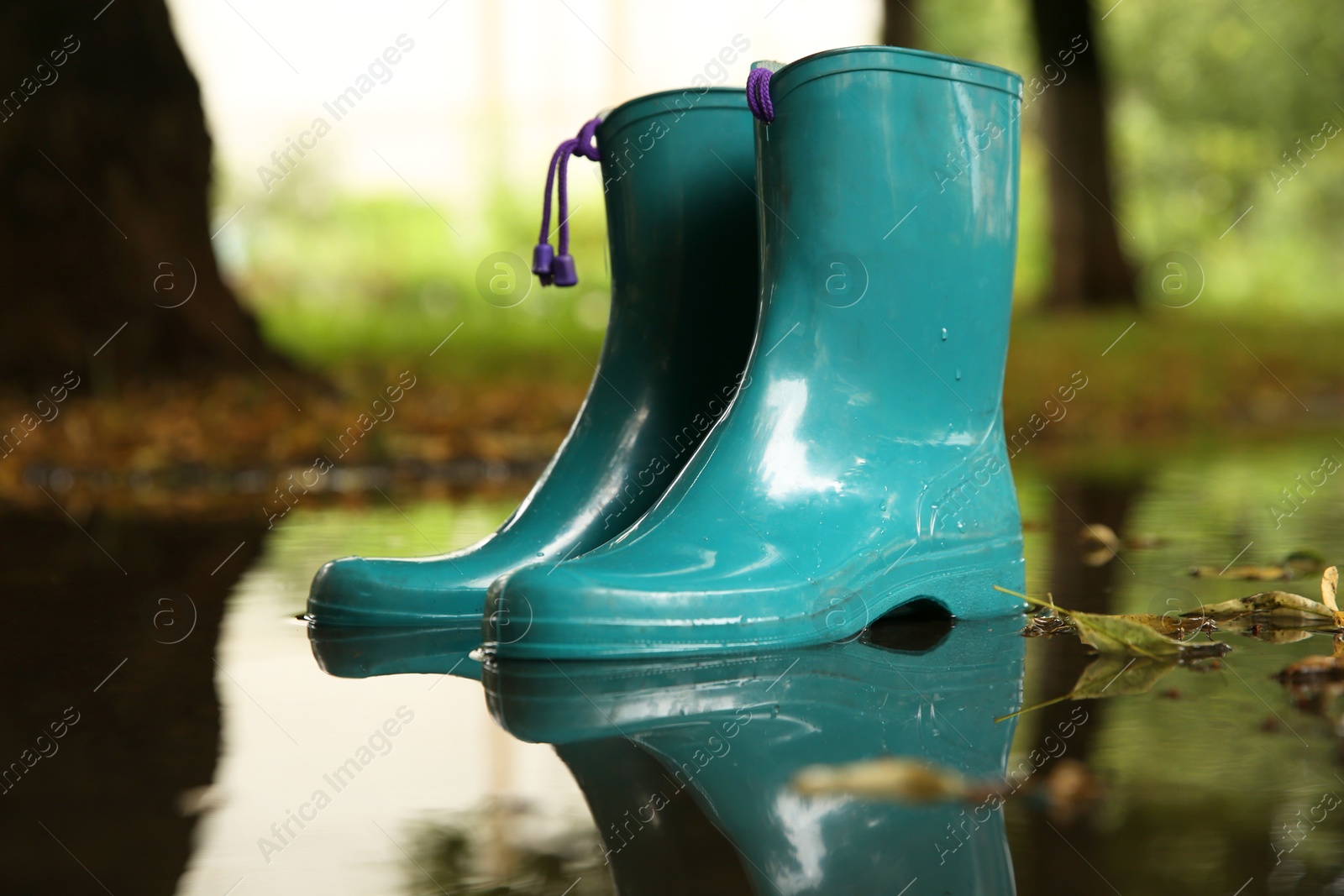 Photo of Pair of colorful rubber boots in puddle outdoors