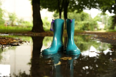 Photo of Pair of colorful rubber boots in puddle outdoors