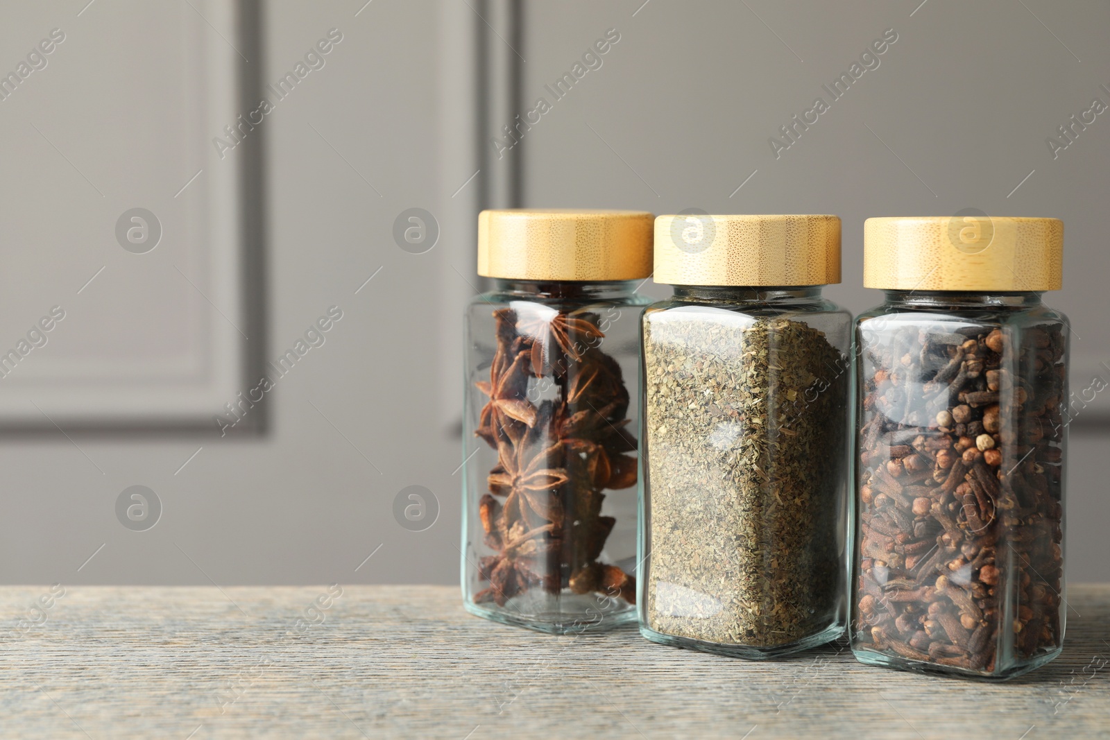 Photo of Different spices in glass jars on wooden table, space for text