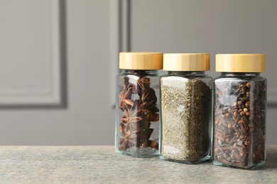 Photo of Different spices in glass jars on wooden table, space for text