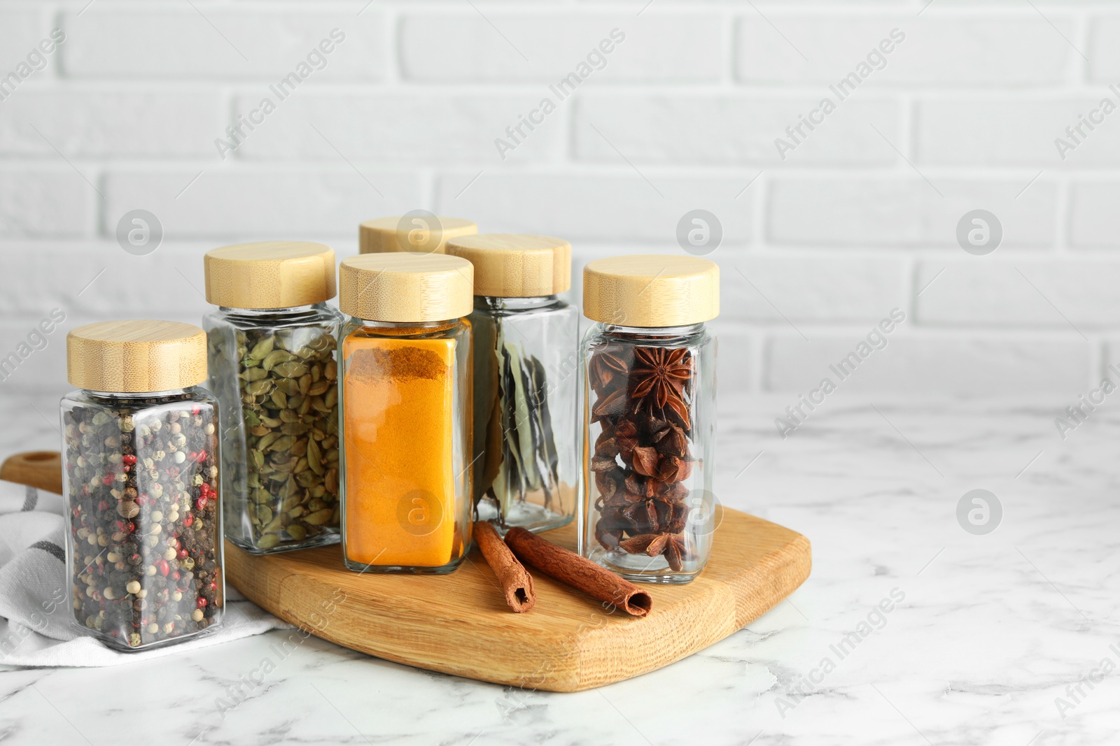 Photo of Different spices in glass jars on white marble table, space for text