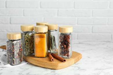 Photo of Different spices in glass jars on white marble table, space for text