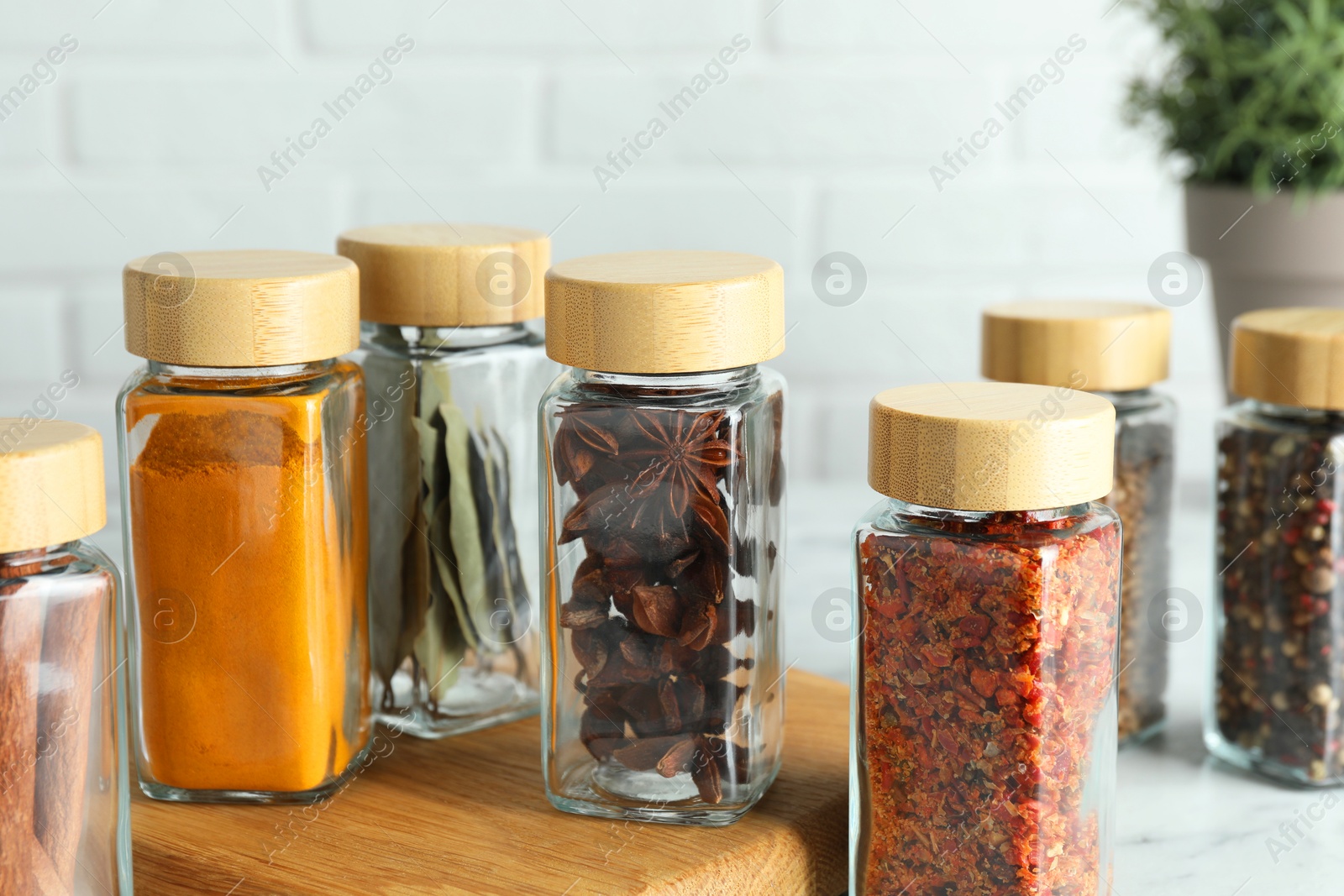 Photo of Different spices in glass jars on white marble table