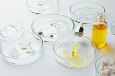 Photo of Petri dishes with different cosmetic products on white background, closeup