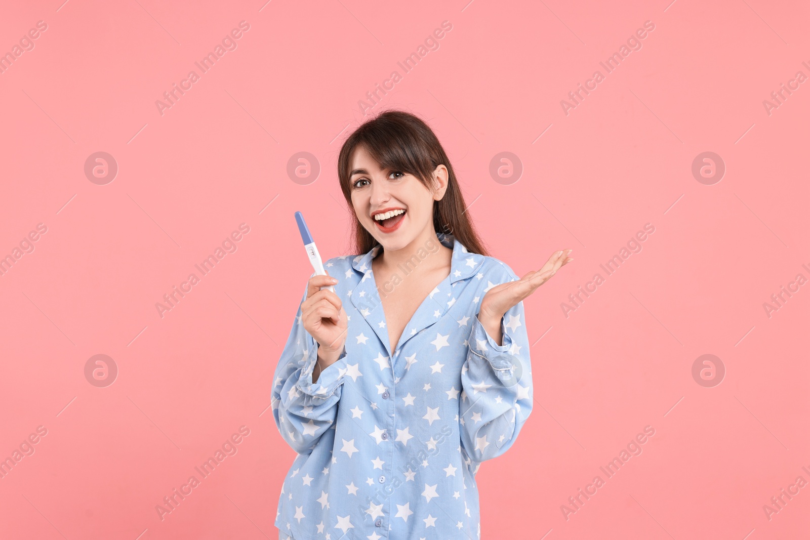 Photo of Happy young woman with pregnancy test on pink background