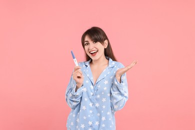 Happy young woman with pregnancy test on pink background