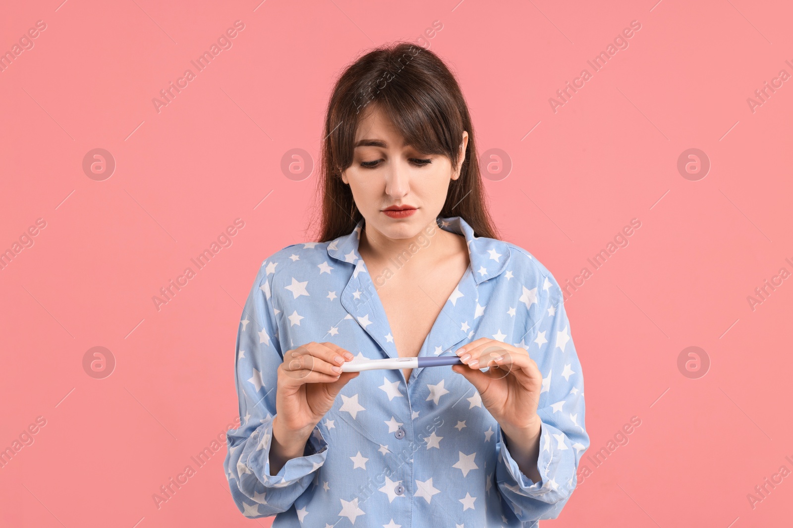 Photo of Worried young woman with pregnancy test on pink background