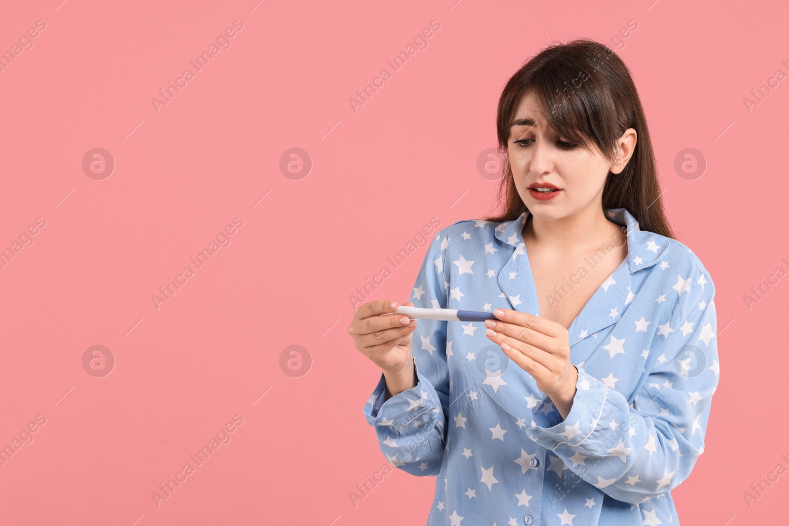 Photo of Worried young woman with pregnancy test on pink background, space for text