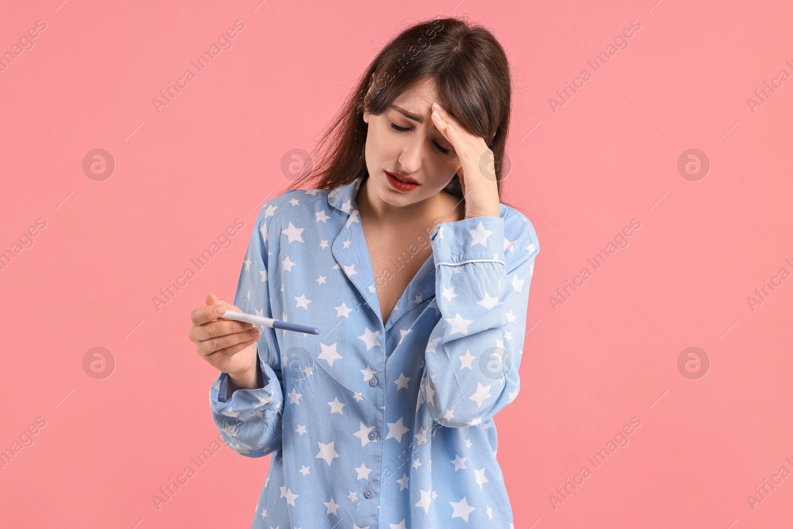 Photo of Worried young woman with pregnancy test on pink background