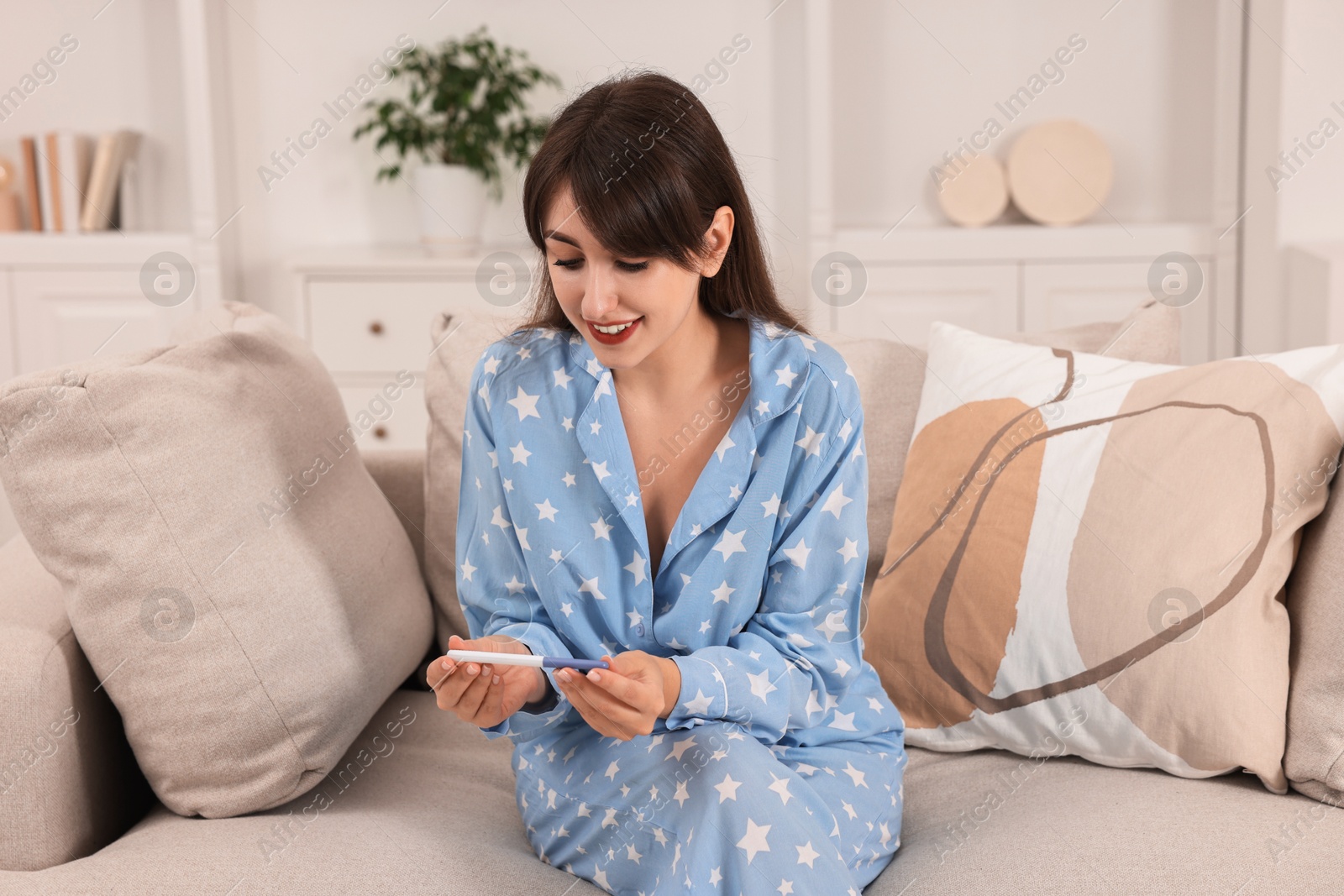 Photo of Happy young woman with pregnancy test on sofa at home