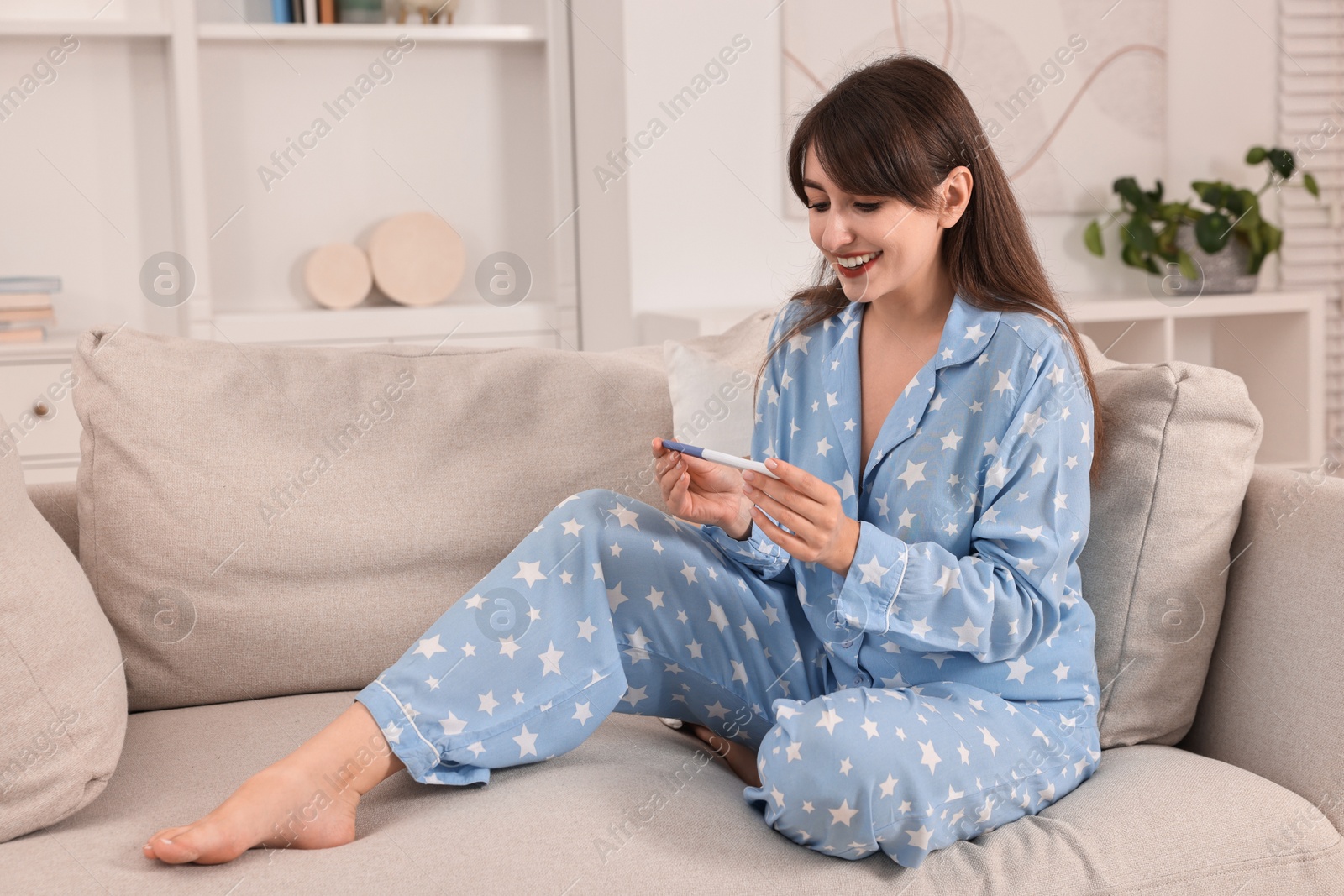 Photo of Happy young woman with pregnancy test on sofa at home