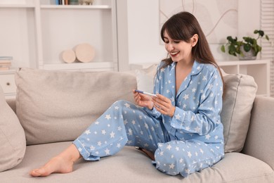 Happy young woman with pregnancy test on sofa at home