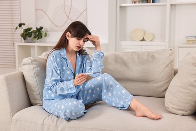 Photo of Worried young woman with pregnancy test on sofa at home