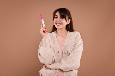 Photo of Happy young woman with pregnancy test on light brown background