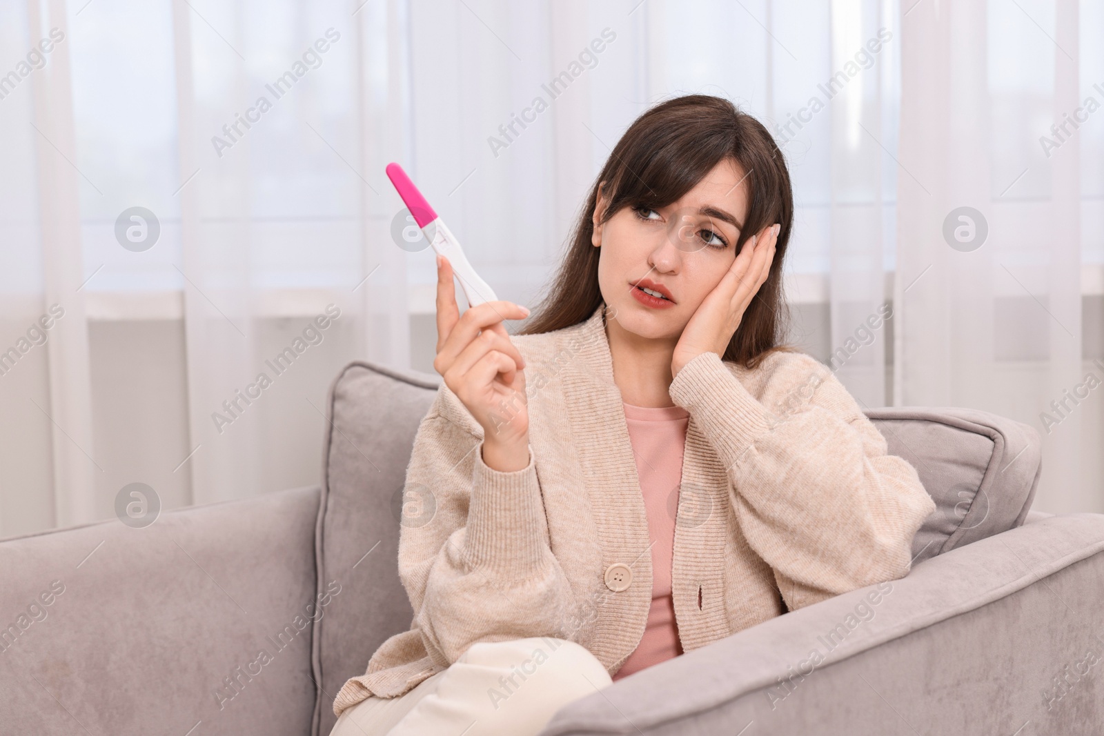 Photo of Worried young woman with pregnancy test on sofa at home