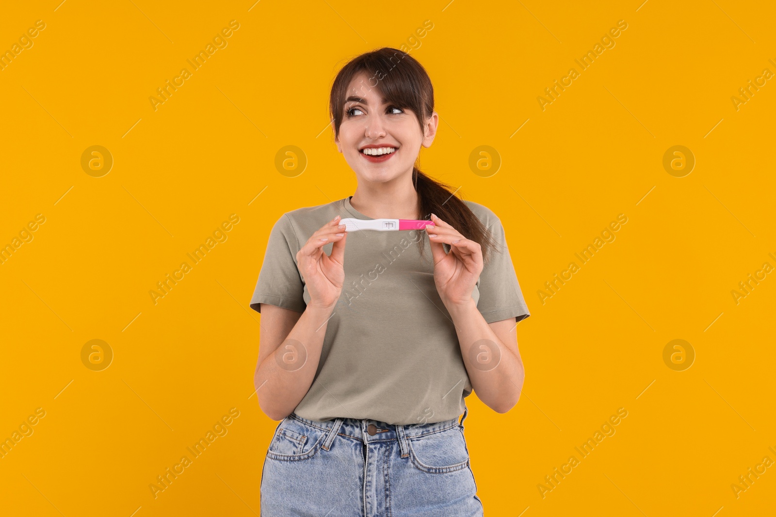 Photo of Happy young woman with pregnancy test on orange background