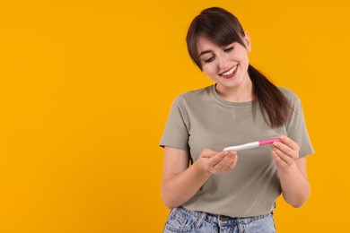 Photo of Happy young woman with pregnancy test on orange background, space for text