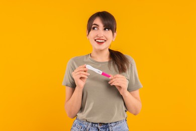 Happy young woman with pregnancy test on orange background