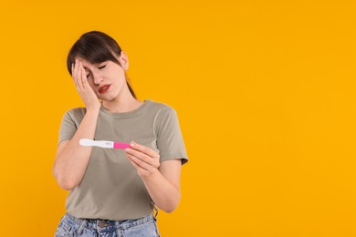 Worried young woman with pregnancy test on orange background, space for text