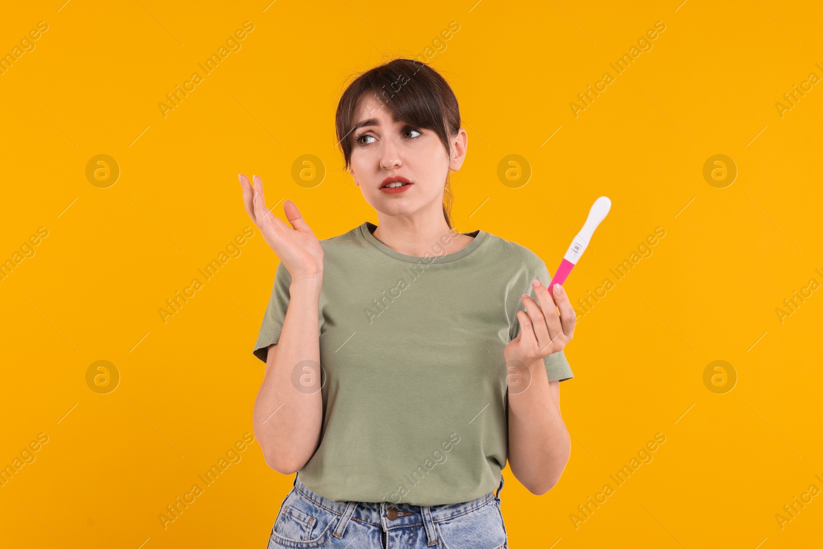 Photo of Worried young woman with pregnancy test on orange background