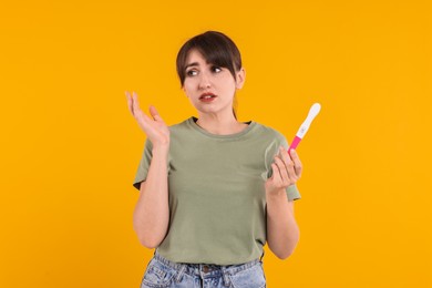 Worried young woman with pregnancy test on orange background