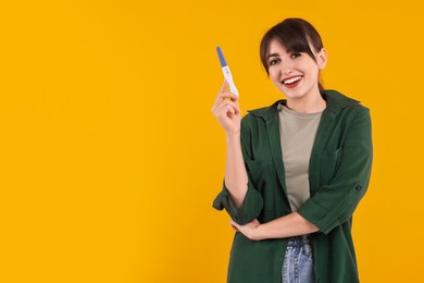 Photo of Happy young woman with pregnancy test on orange background, space for text