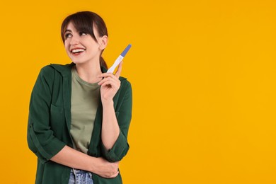 Photo of Happy young woman with pregnancy test on orange background, space for text