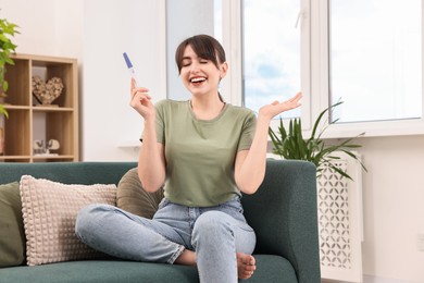 Happy young woman with pregnancy test on sofa at home