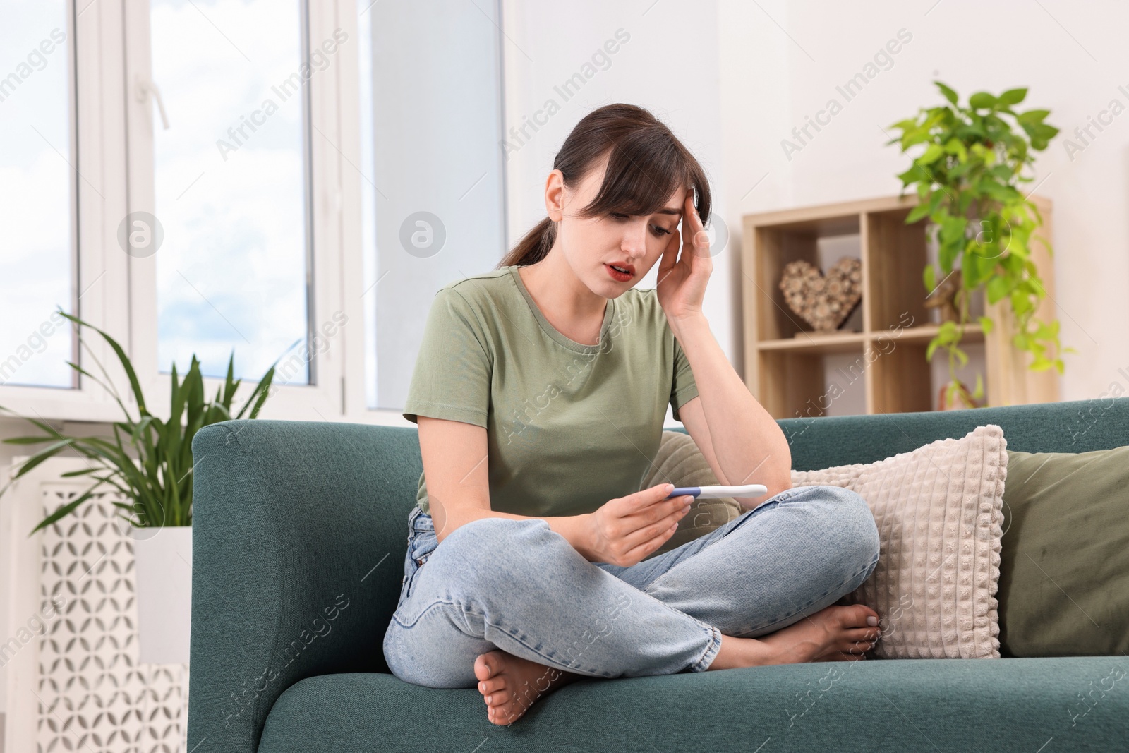 Photo of Worried young woman with pregnancy test on sofa at home